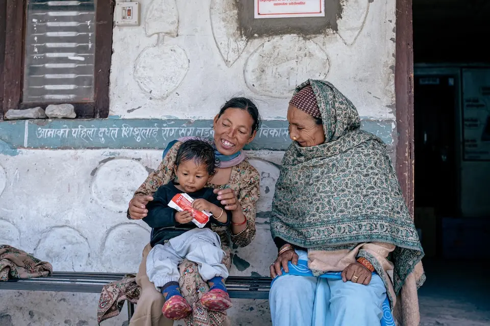 Sitting on his mother's lap in Nepal, a severely malnourished child holds a packet of ready-to-use therapeutic food.  