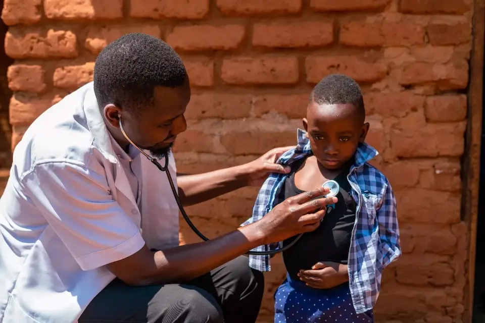 A health worker holds a stethoscope to a young child's chest.