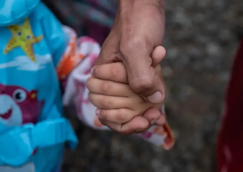 A girl holds her father's hand after they navigated the Darien Gap after fleeing Venezuela.