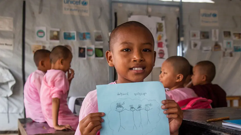 Smiling girl holding up a drawing in school