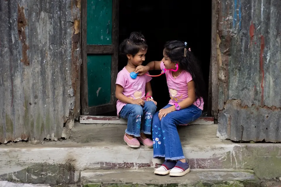 A girl uses a toy stethoscope to check her sister's heartbeat in Bangladesh.