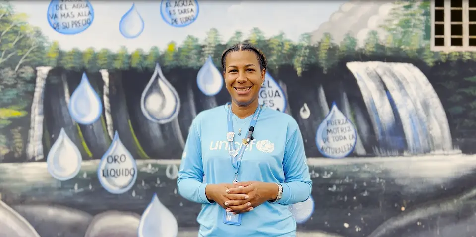 Woman smiling at camera wearing long sleeve unicef tee shirt, standing in front of a mural of waterfall and water droplets