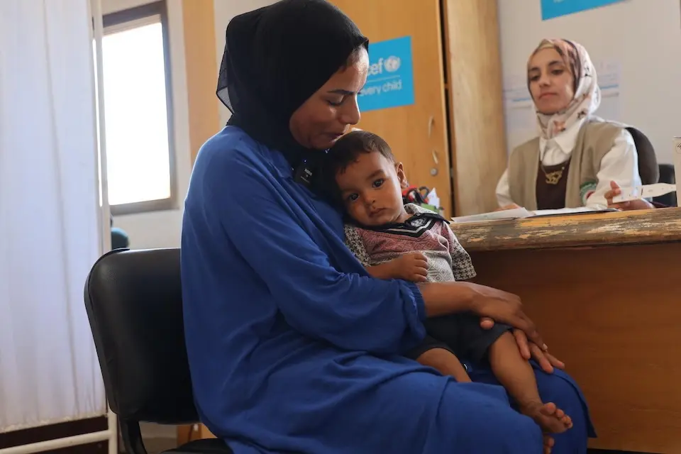 A mother holds her baby son on her lap at a UNICEF-supported health clinic in the Gaza Strip.