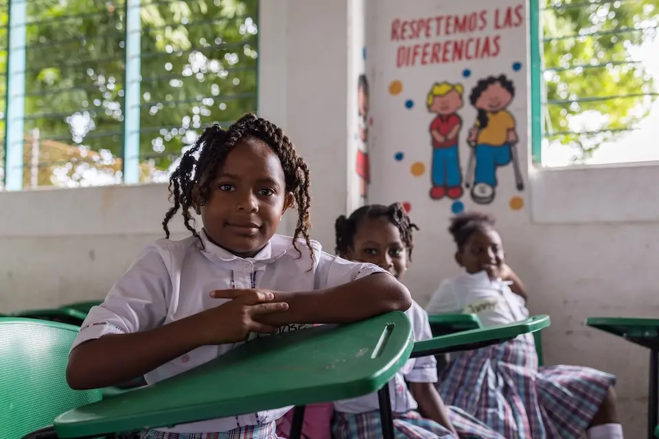 Students sit at desks in a school in Colombia, with a disability rights poster on the wall. 