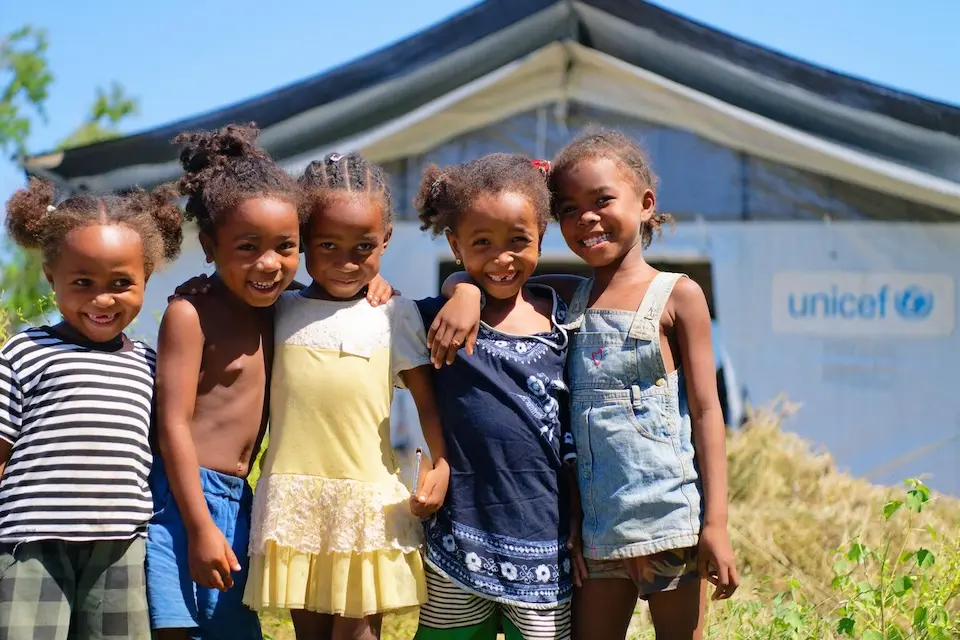 A group of smiling girls stands in front of their temporary learning space in Madagascar, constructed by UNICEF