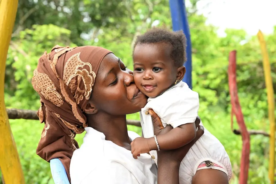Woman kissing the cheek of baby she is holding up, both smiling