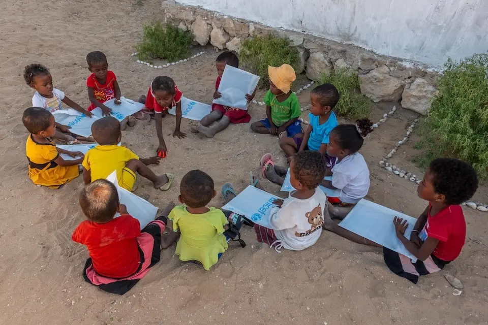Schoolchildren in Madagascar sit on the ground with learning materials supplied by UNICEF.