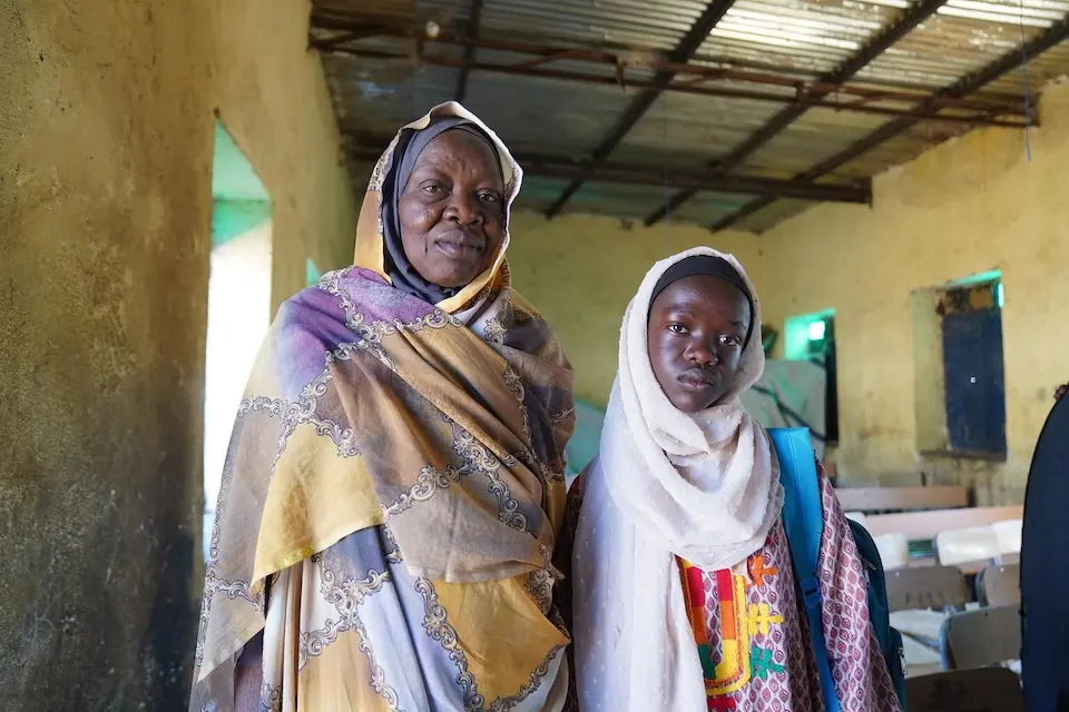 A mother and teacher stands with one of her students in a UNICEF-supported school that doubles as her workplace and home.