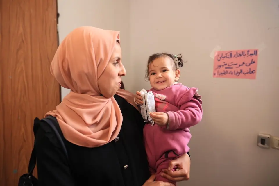 In the Gaza Strip, a mother holds her baby daughter at a site where UNICEF distributes nutrition supplies to children and pregnant women. 