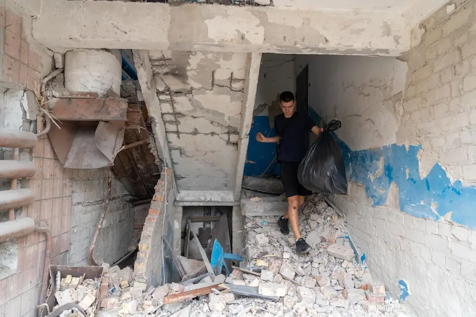 On Sept. 1, 2026, a resident carries belongings through the heavily damaged entrance of an apartment building in Boryspil, Kyiv region, Ukraine, following an overnight attack. 