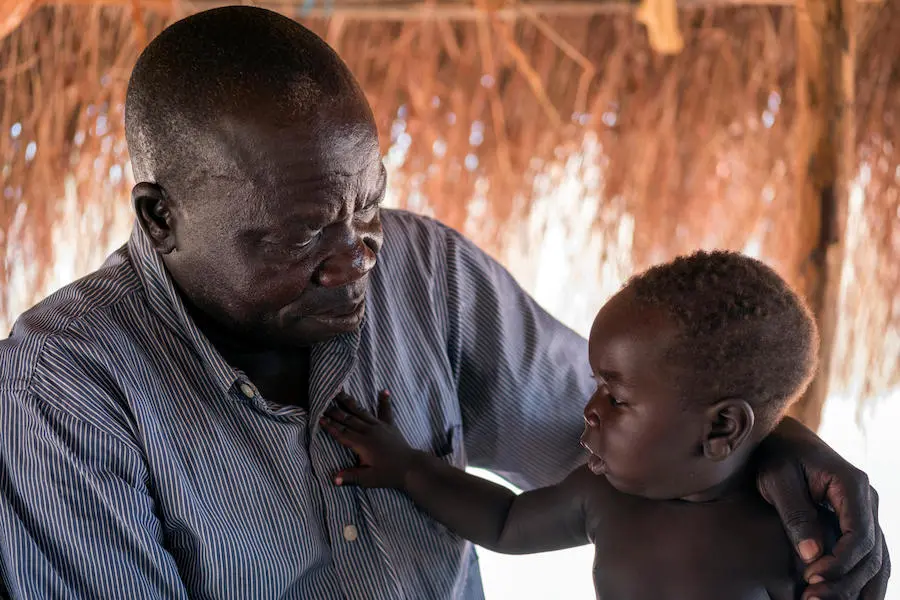 South Sudanese refugee Abura Silvano with his 6-month-old son, Luke Given, outside their shelter in Bidi Bidi refugee settlement in northern Uganda. unicef, father's day, south sudanese refugees, bidi bidi, refugees, south sudan, uganda