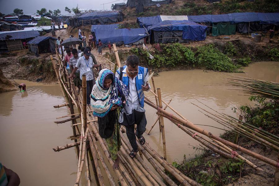 Carryin her newborn granddaughter, Johora, accompanied by a volunteer health worker, crosses a rickety bamboo bridge in the sprawling Kutupalong camp for Rohingya refugees in Cox's Bazar, Bangladesh.