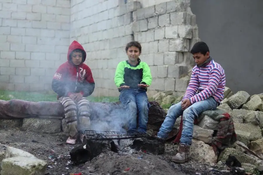 Mohammad, 13, (right) and his sister Mehdia, 9, gather around a fire to warm up with their neighbor Sami. Mohammad, 13, (right) and his sister Mehdia, 9, gather around a fire to warm up with their neighbor Sami.
