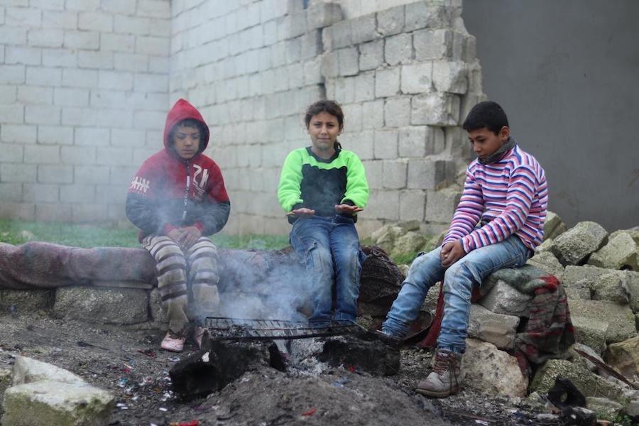 Mohammad, 13, (right) and his sister Mehdia, 9, gather around a fire to warm up with their neighbor Sami.