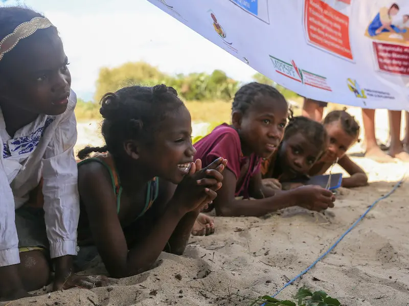 Children in Tanandava, Madagascar listen as UNICEF-trained Mother Leaders sing an educational song in 2019. Children in Tanandava, Madagascar listen as UNICEF-trained Mother Leaders sing an educational song in 2019.