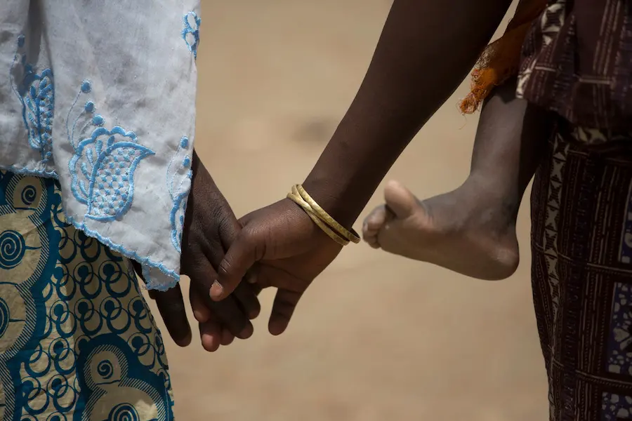 A girl walks with her mother while carrying her sister at a camp for refugees from the Boko Haram insurgency in Camaroon.