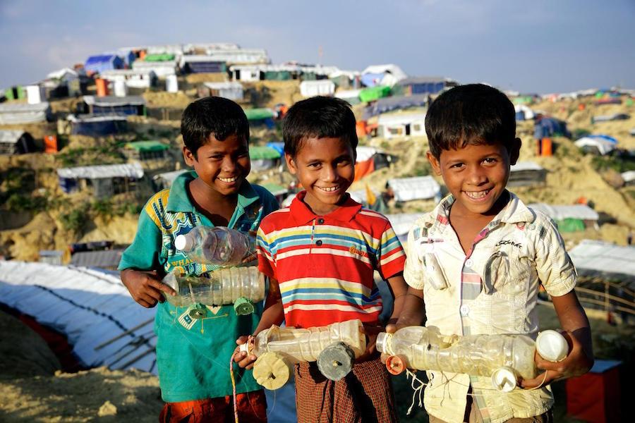In December 2017 in Bangladesh, three smiling boys hold toy cars they made from discarded objects in a makeshift Rohingya refugee settlement in Ukhia sub-district, in Cox’s Bazar district.