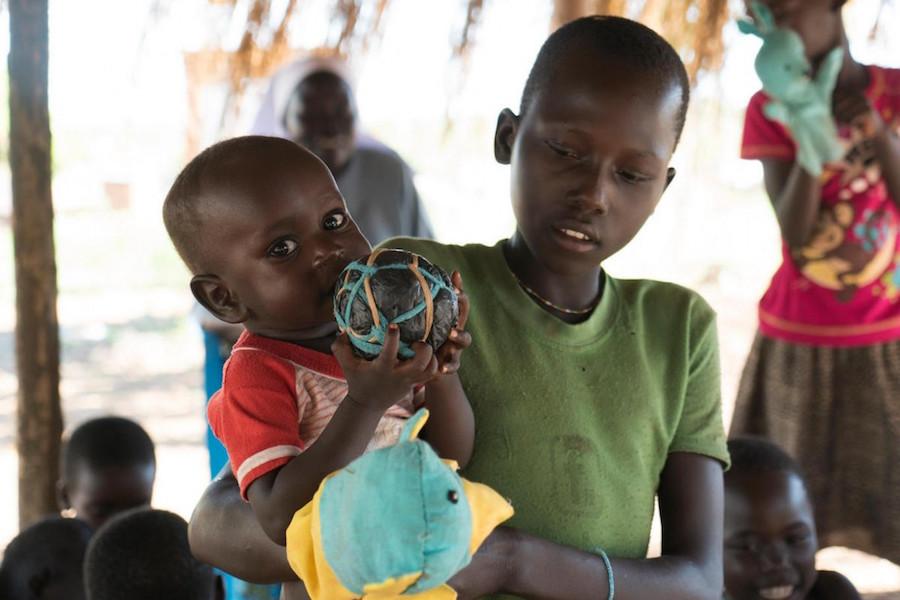 Carried by her older sister, a baby plays with a homemade ball in Bidi Bidi, a refugee camp in northern Uganda's West Nile region in May 2018. 