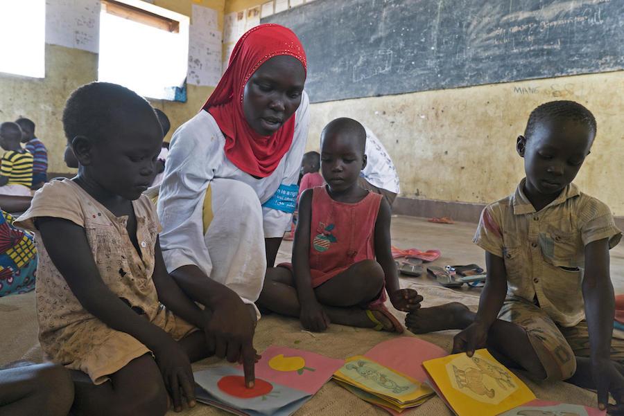 Ugandan caregiver Dalla Alli, 28, shows locally made cardboard books to South Sudanese refugee children in Bidi Bidi refugee settlement. 