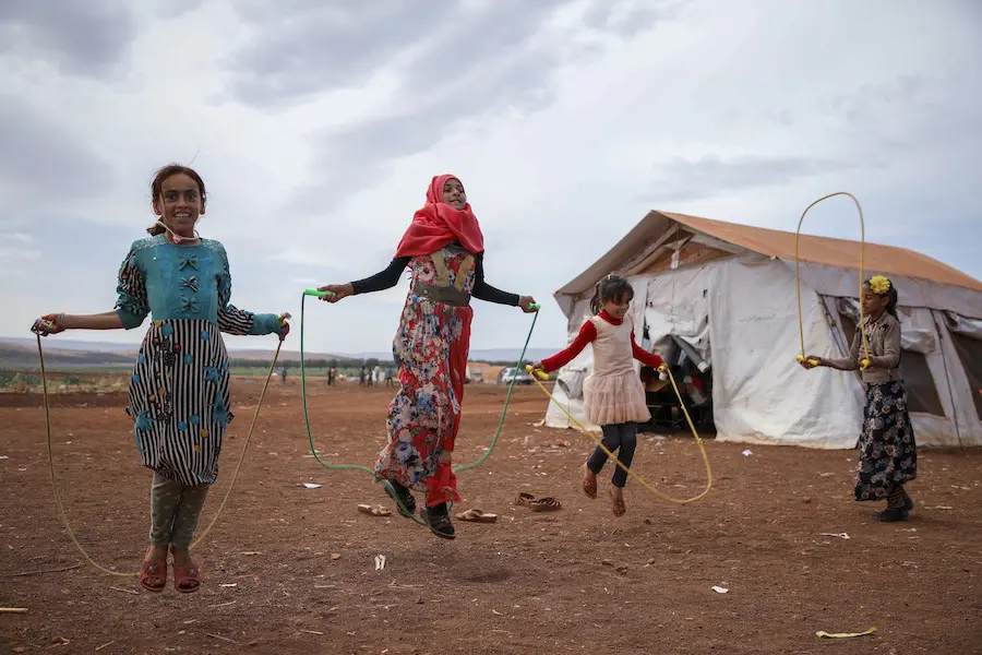 Girls jump rope outside temporary classrooms at a Syrian camp for displaced families. Girls jump rope outside temporary classrooms at a Syrian camp for displaced families.