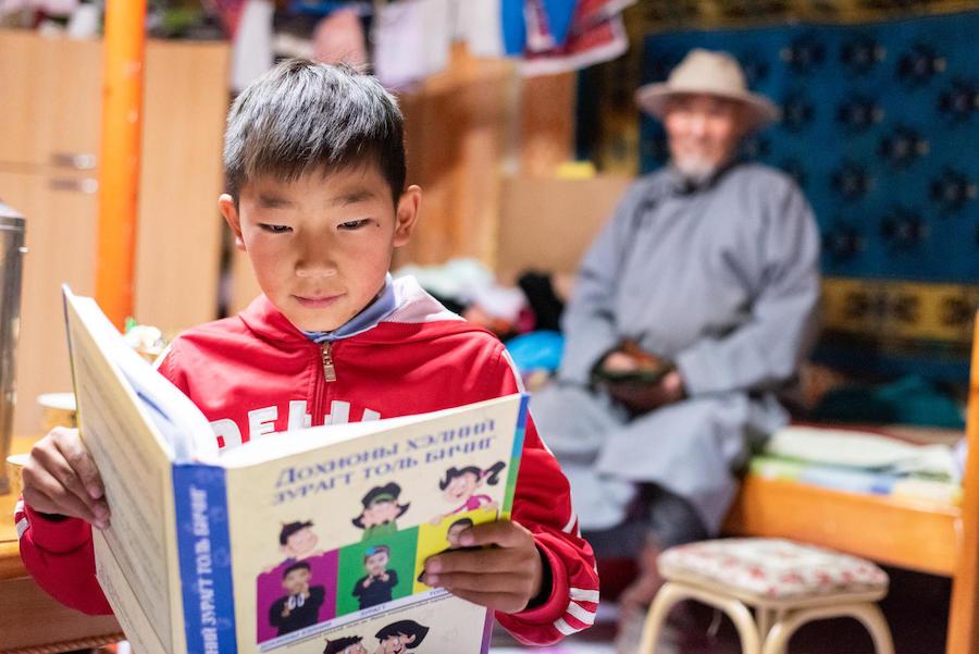 A special needs student reads a book at his house in Altai, Gobi-Altai province, Mongolia in September 2018. UNICEF has developed a sign language book for deaf children. 