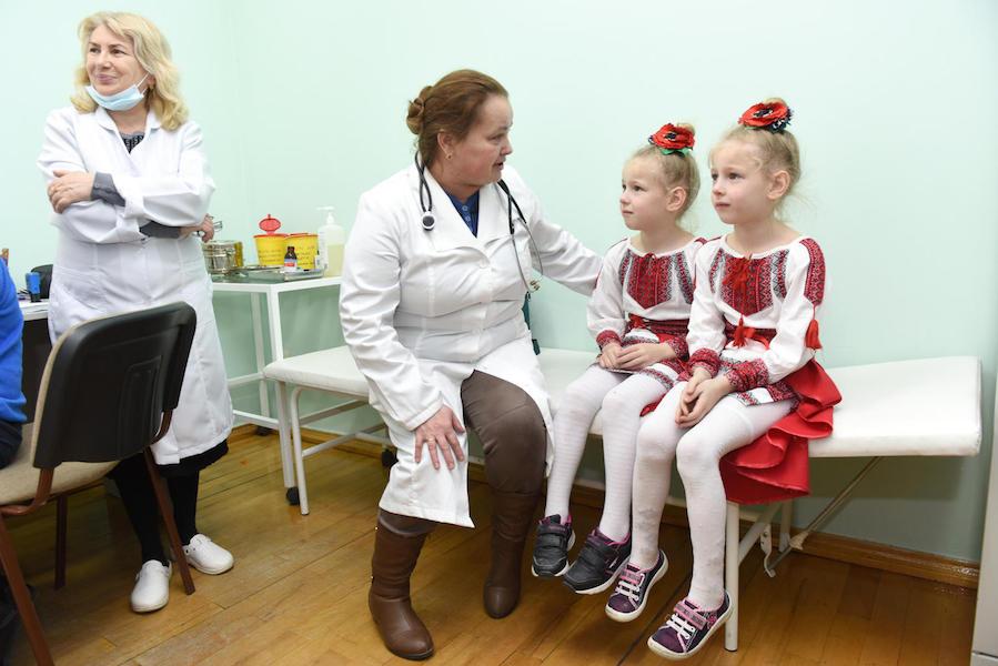 A UNICEF-supported health worker comforts 6-year-old sisters Vitalina and Yuliana before their measles, mumps and rubella vaccination in February 2019 in the Lapaivka village school in western Ukraine's Lviv region. 