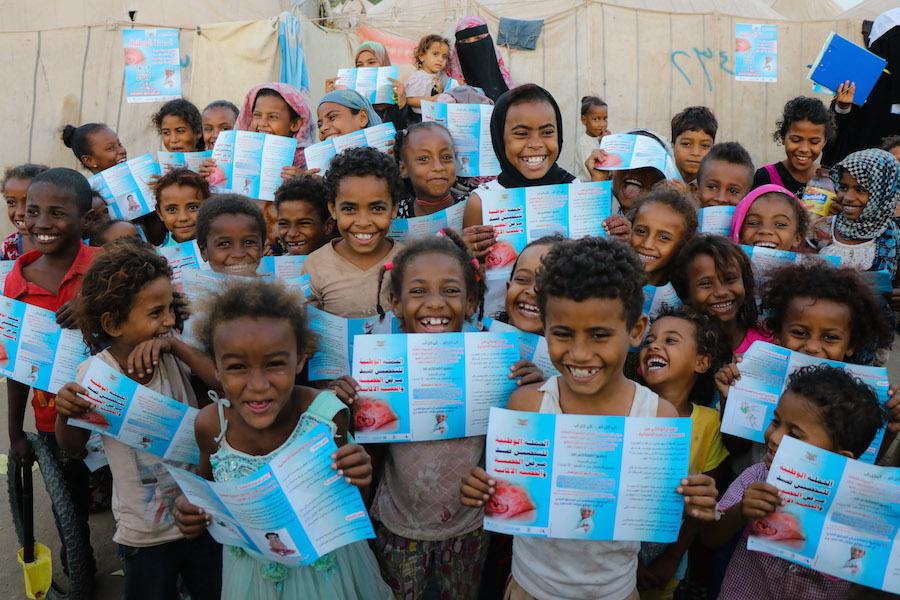 Kids in Aden, Yemen, hold up a UNICEF provided brochure that explains the safety and efficacy of the measles and rubella vaccine kids need to stay healthy. 