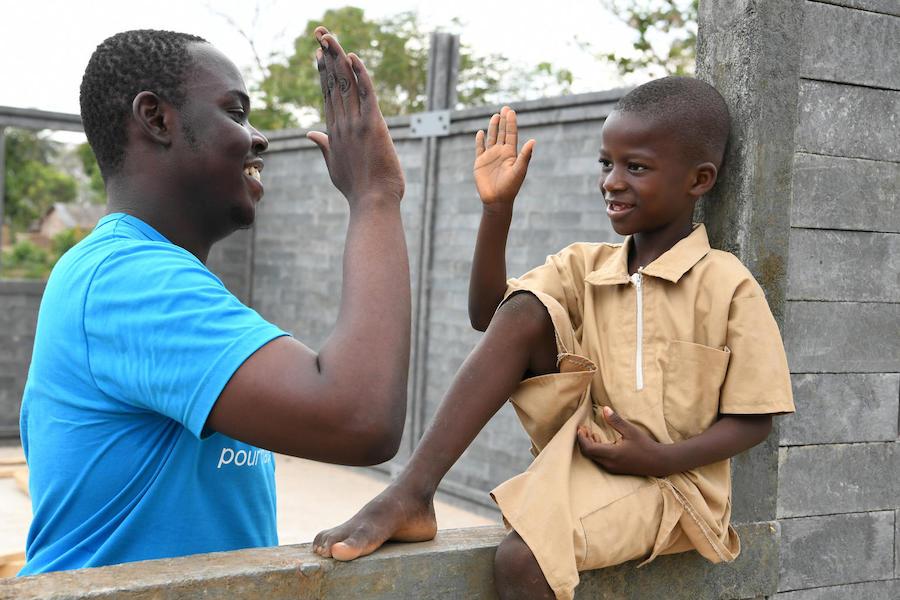 In February 2019, UNICEF staff member Stéphane Gbonikan and a student high five on the site of a new classroom built of recycled plastic bricks in Sakassou, Côte d'Ivoire. 