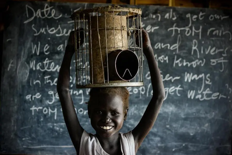 Six-year-old Nyaboth holds her family stove in Bentiu Protection of Civilians site in Unity State, South Sudan in 2016. Nyaboth carries the stove to school every day so she has something to sit on while she learns. UNICEF, South Sudan, South Sudanese refugees