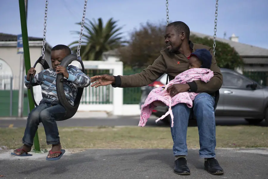 Dieu-Merci Matala, 44, holds his 7-month-old daughter, Grace, while pushing his 4-year-old son, Joshua on the swing in Maitland, Cape Town, South Africa in May 2019. Dieu-Merci Matala, 44, holds his 7-month-old daughter, Grace, while pushing his 4-year-old son, Joshua on the swing in Maitland, Cape Town, South Africa in May 2019.