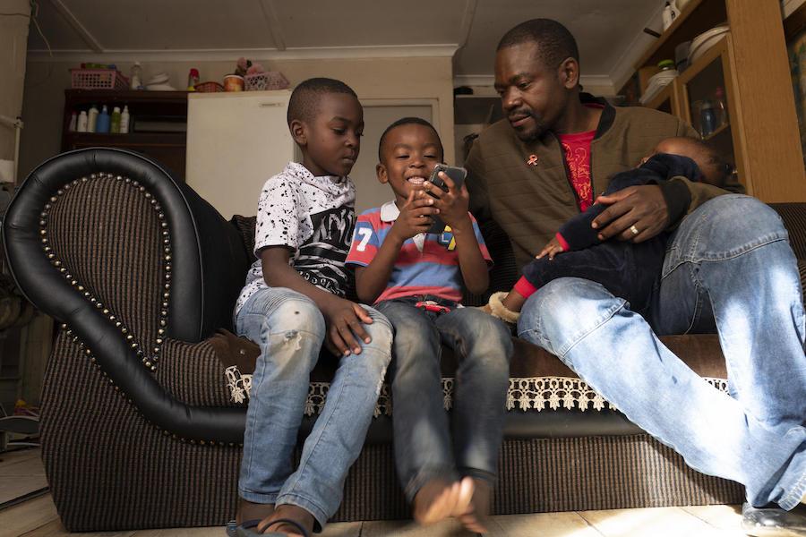 Dieu-Merci Matala, 44, holds his 7-month-old daughter, Grace, while her brothers David, 7 (far left), and Joshua, 4, play in the family's apartment in Maitland, Cape Town, South Africa in May 2019.