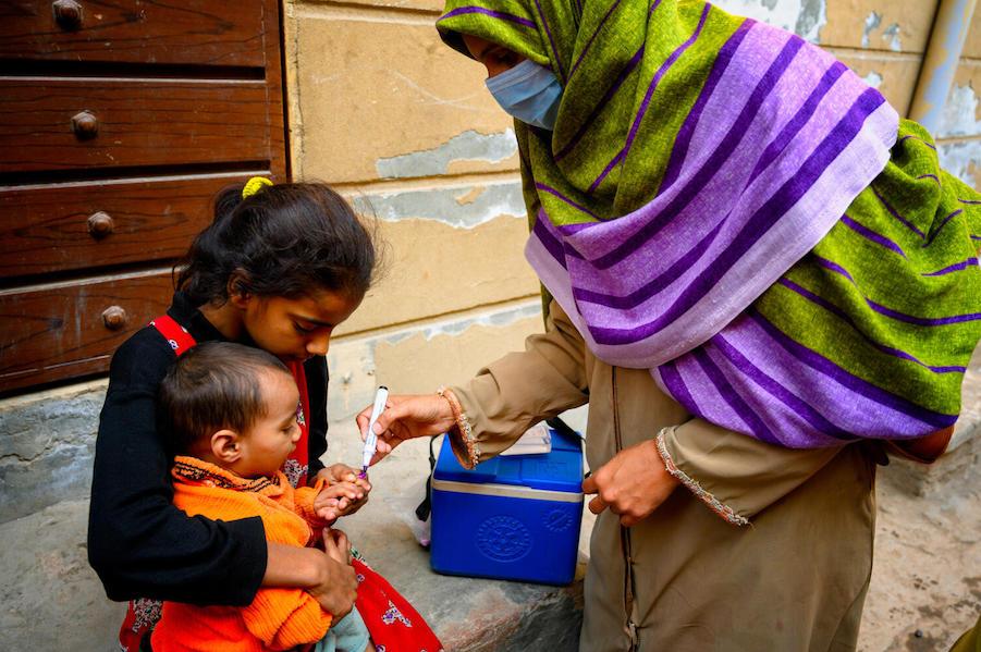 In January 2021, Shumaila, a polio vaccinator in Lahore, Pakistan, marks the finger of an 18-month old boy with the help of his sister, to show that he has received his vaccination.