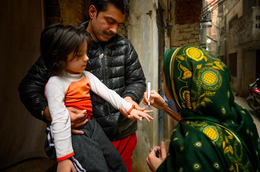 In January 2021, Sumaira, a polio vaccinator in Lahore, Pakistan, marks the finger of a 4-year-old with the help of the girl's father after vaccinating her with polio and giving her Vitamin A supplementation.