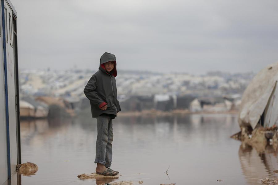 On 19 January 2021, a child stands on a dry patch surrounded by floodwater in Kafr Losin Camp in northwest Syrian Arab Republic.