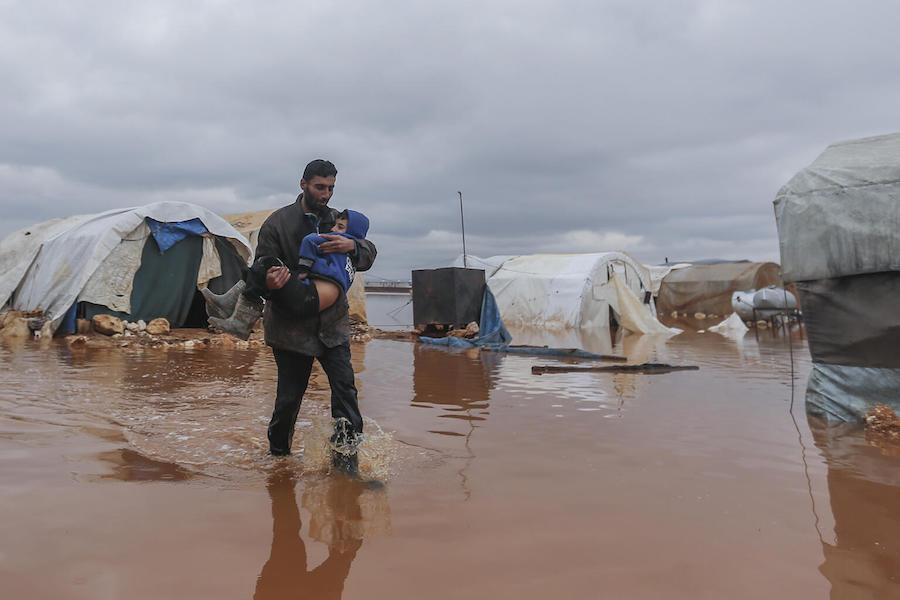 On 19 January 2021, Abu Qutaiba carries his 11-year-old son, Kamel, through a flooded area in Kafr Losin Camp in northwest Syrian Arab Republic.