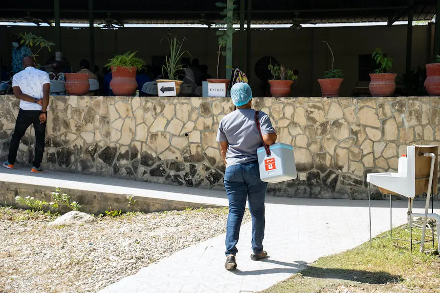 A nurse carries COVID-19 vaccines from a UNICEF solar-powered fridge to a hospital vaccination site in Port-au-Prince, Haiti. A nurse carries COVID-19 vaccines from a UNICEF solar-powered fridge to a hospital vaccination site in Port-au-Prince, Haiti.