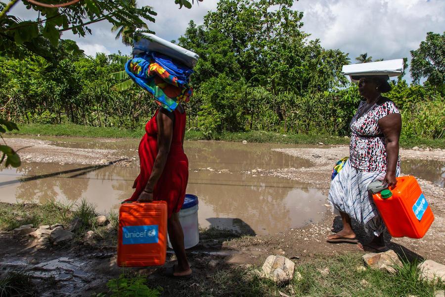 On August 18, 2021, Mera Marie Malia, a 38-year-old mother of five and seven months pregnant, left, and her neighbor, carry UNICEF-distributed supplies including tarpaulins and essential hygiene items, in Valere in Haiti’s Sud Department.