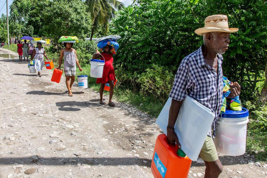 On August 18, 2021, Mera Marie Malia, a 38-year-old mother of five (center, in red) and her neighbors receive an emergency kit containing tarpaulins and essential hygiene supplies in Valere, a village in Haiti’s Sud Department.