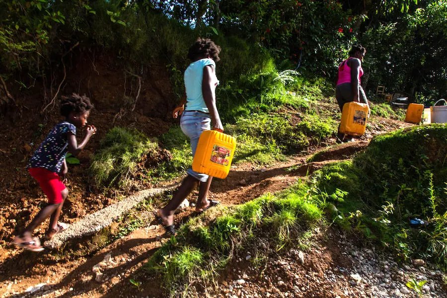 On August 18 2021, in Marceline, near Haiti's Camp Perrin district, 7-year-old Farah Figaro, collects water at one of the four water stations supported by UNICEF in Les Cayes. On August 18 2021, in Marceline, near Haiti's Camp Perrin district, people carry jerry cans of water from one of the four water stations supported by UNICEF in Les Cayes.