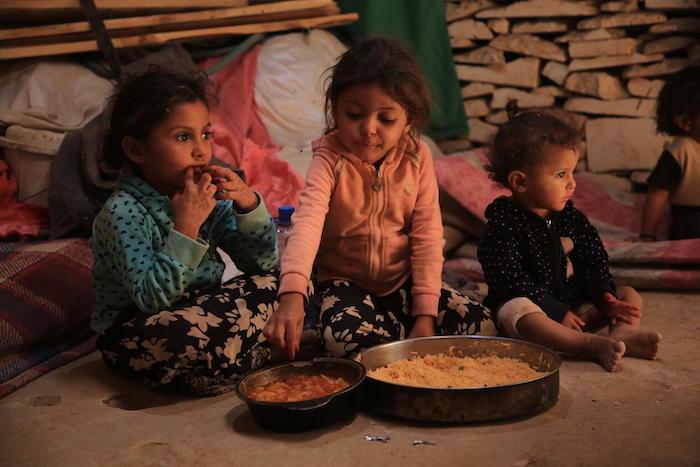 Three children eat a meal with their family inside of Al-Jufainah camp, Marib, Yemen. 