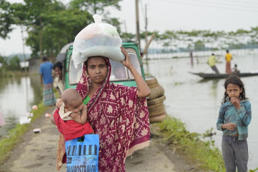 A woman with her baby carries emergency supplies back to their flooded village in Sylhet, Bangladesh on May 23, 2022.