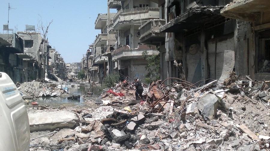 #SyriaCrisis a woman traverses a debris-covered street n the Old City area of Homs, Syria.