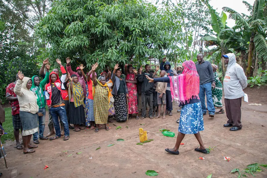 Standing on a homemade map showing the nearest open defecation spots, schools, health centers and water sources, a UNICEF-trained health worker discusses open defecation with community members in western Uganda's Kamwenge district in 2019. Standing on a homemade map showing the nearest open defecation spots, schools, health centers and water sources, a UNICEF-trained health worker discusses open defecation with community members in western Uganda's Kamwenge district in 2019.