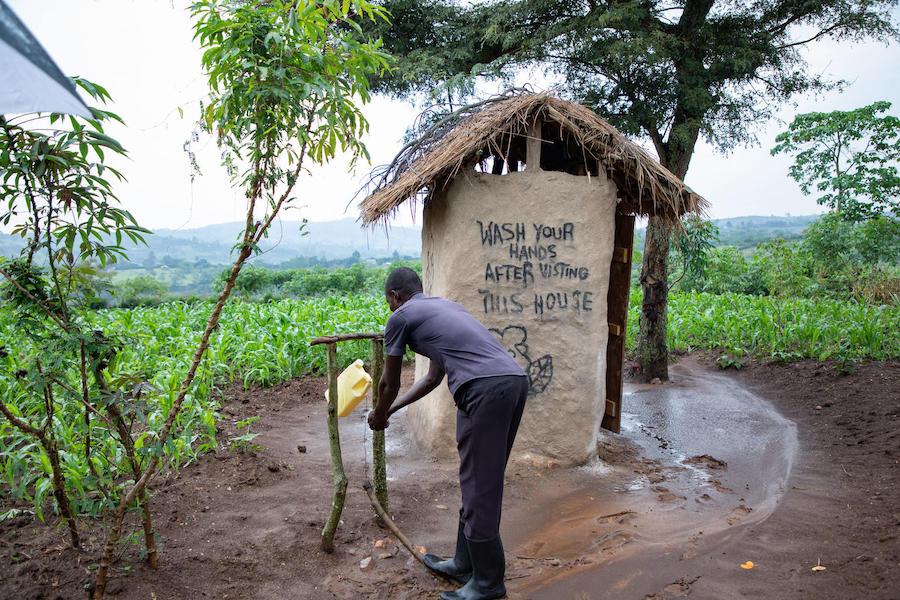 Nsemirirwe Aarons washes his hands outside his family's latrine in western Uganda's Kamwenge district. They added the tippy tap after attending a UNICEF education session in 2019. 