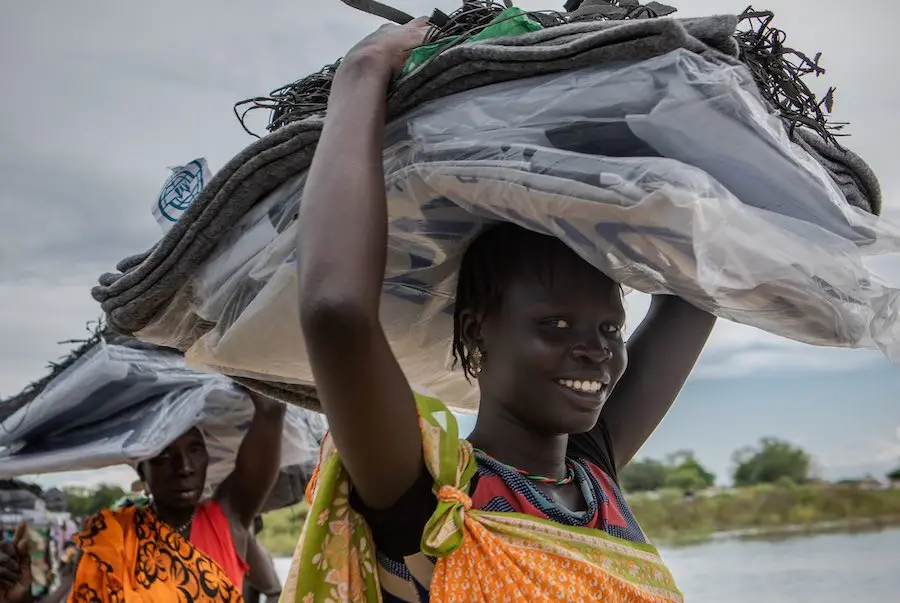 Community members carry a load of non-food items, such as blankets and tarpaulin, distributed by NGOS, following devestating flooding, in Pibor, Boma State, South Sudan, on 6 November 2019 // Photo credit: UNICEF South Sudan/de la Guardia Community members carry a load of non-food items, such as blankets and tarpaulin, distributed by NGOS, following devestating flooding, in Pibor, Boma State, South Sudan, on 6 November 2019 // Photo credit: UNICEF South Sudan/de la Guardia