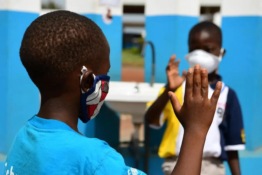 Two young friends greet each other from safe distance as required by COVID-19 prevention measures. Two young friends greet each other from a safe distance as required by COVID-19 prevention measures.