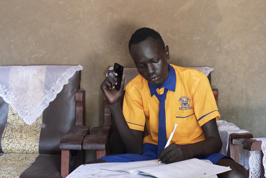 In June 2020 in South Sudan, George, 17, listens to a NICEF-supported radio lesson on his phone while schools are closed to prevent the spread of the novel coronavirus.