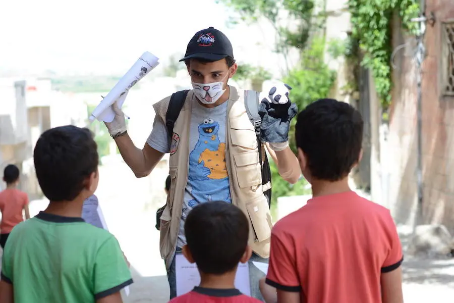 In northern rural Homs, Syria on May 14, 2020, children listen raptly to UNICEF-supported volunteer Salam, who goes door-to-door providing activities and health information to children during the COVID-19 lockdown. In northern rural Homs, Syria on May 14, 2020, children listen raptly to UNICEF-supported volunteer Salam, who goes door-to-door providing activities and health information to children during the COVID-19 lockdown.