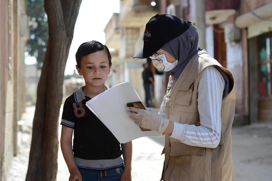 On May 14, 2020, UNICEF-supported volunteer Aya, 24, talks with a boy about COVID-19 in the war-ravaged village of Teir-Ma'aleh, Homs, Syria. 