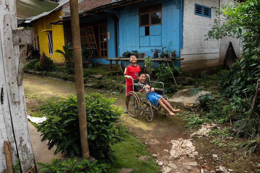 Kevin, 9, a child with a visual impairment, pushes his 12-year-old friend Syaiful's wheelchair as they play outside in Banyumas, Central Java, Indonesia. Kevin, 9, a child with a visual impairment, pushes his 12-year-old friend Syaiful's wheelchair as they play outside in Banyumas, Central Java, Indonesia.
